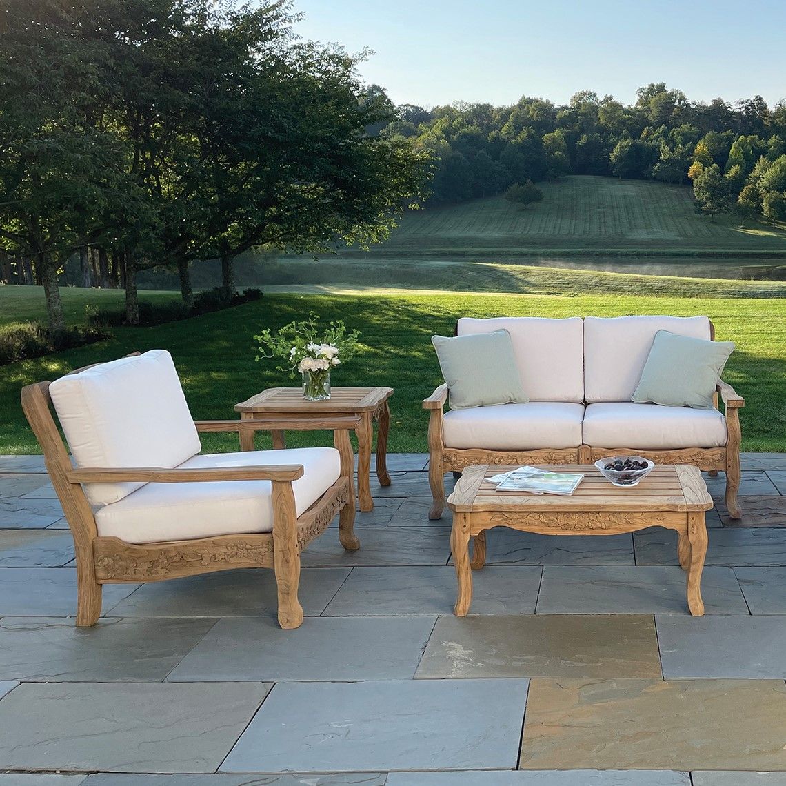 The Normandy Coffee Table showcases exceptional craftsmanship with hand-carved hummingbird and trumpet vine reliefs in weather-resistant distressed teak. Its compact 36-inch size fits intimate outdoor seating areas beautifully. - alternate view